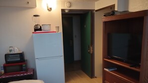 Kompakti hotellihuone, jossa on sänky, pieni keittonurkkaus, jossa on mikroaaltouuni ja leivänpaahdin, jääkaappi, televisio ja puinen kaappi.