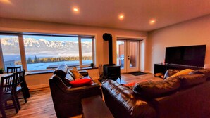 A living room with a large window offering a mountain view, a fireplace, a sofa, and a television. - Stay Golden - Monashee House (Golden)