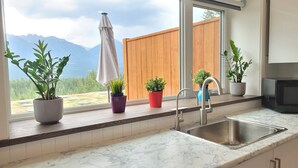 A kitchen with a large window, a sink, and potted plants. - Stay Golden - Monashee House (Golden)