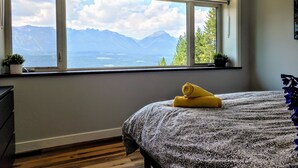 Een slaapkamer met een groot raam met uitzicht op bergen en een meer.