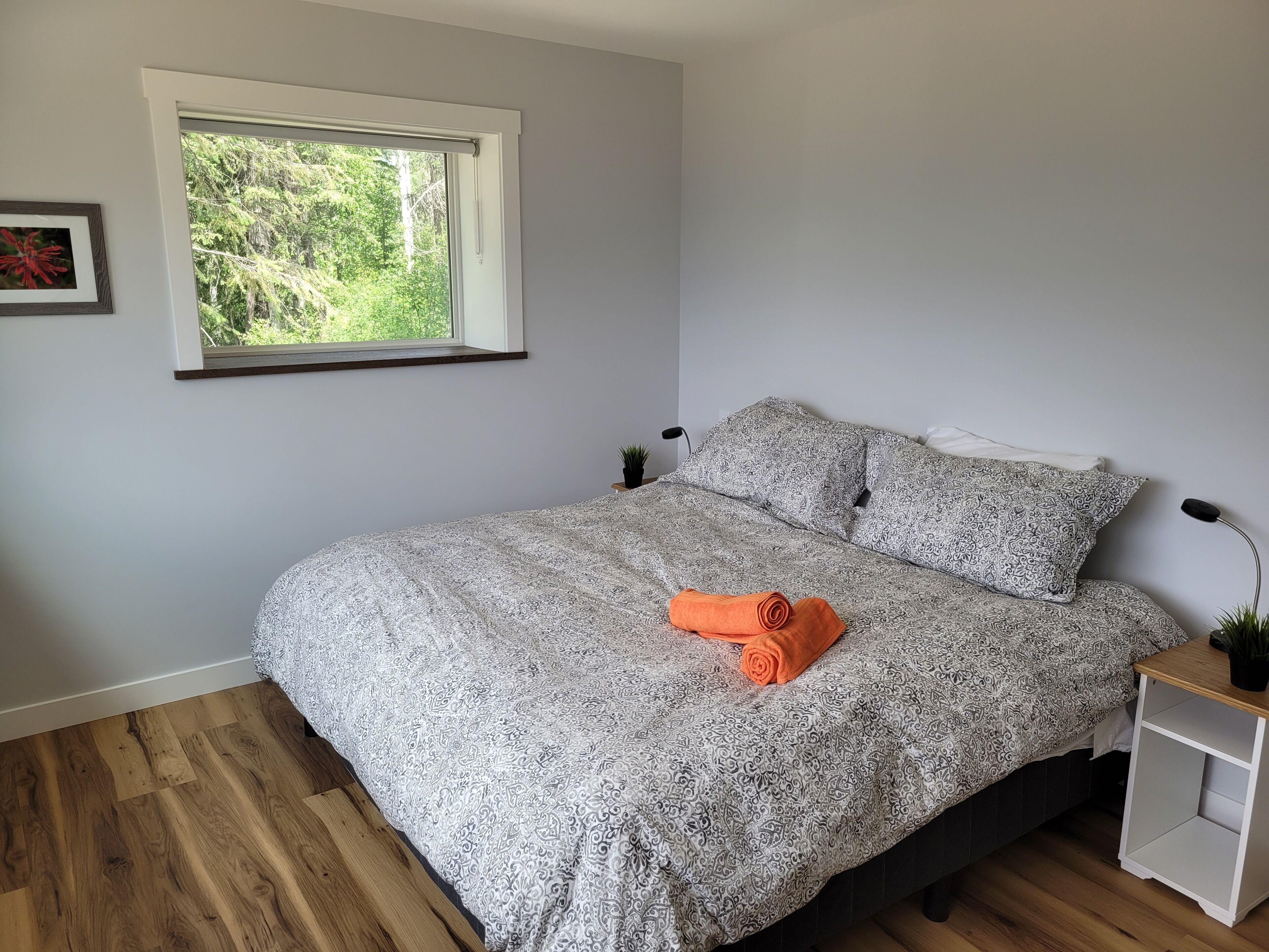A bedroom with a bed, a window, a small bedside table, and a framed picture on the wall.