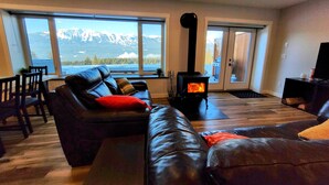 Un salon avec un canapé en cuir, une cheminée et une vue sur les montagnes, visible à travers de grandes fenêtres.
