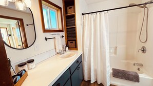 A bathroom with a sink, mirror, towel rack, shower curtain, and a shelf with baskets. - Updated Farmhouse with lots of outdoor space and beautiful views! (Linn County)