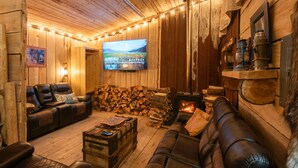 A cozy cabin interior with wooden walls, a fireplace, a television, and leather seating.