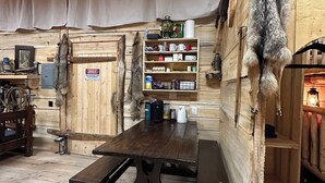 A rustic interior with wooden walls, a wooden table, and shelves with various items.
