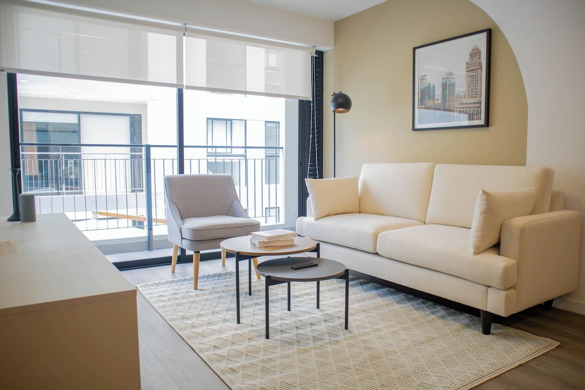 A modern living room with a sofa, armchair, coffee table, and a cityscape painting on the wall.