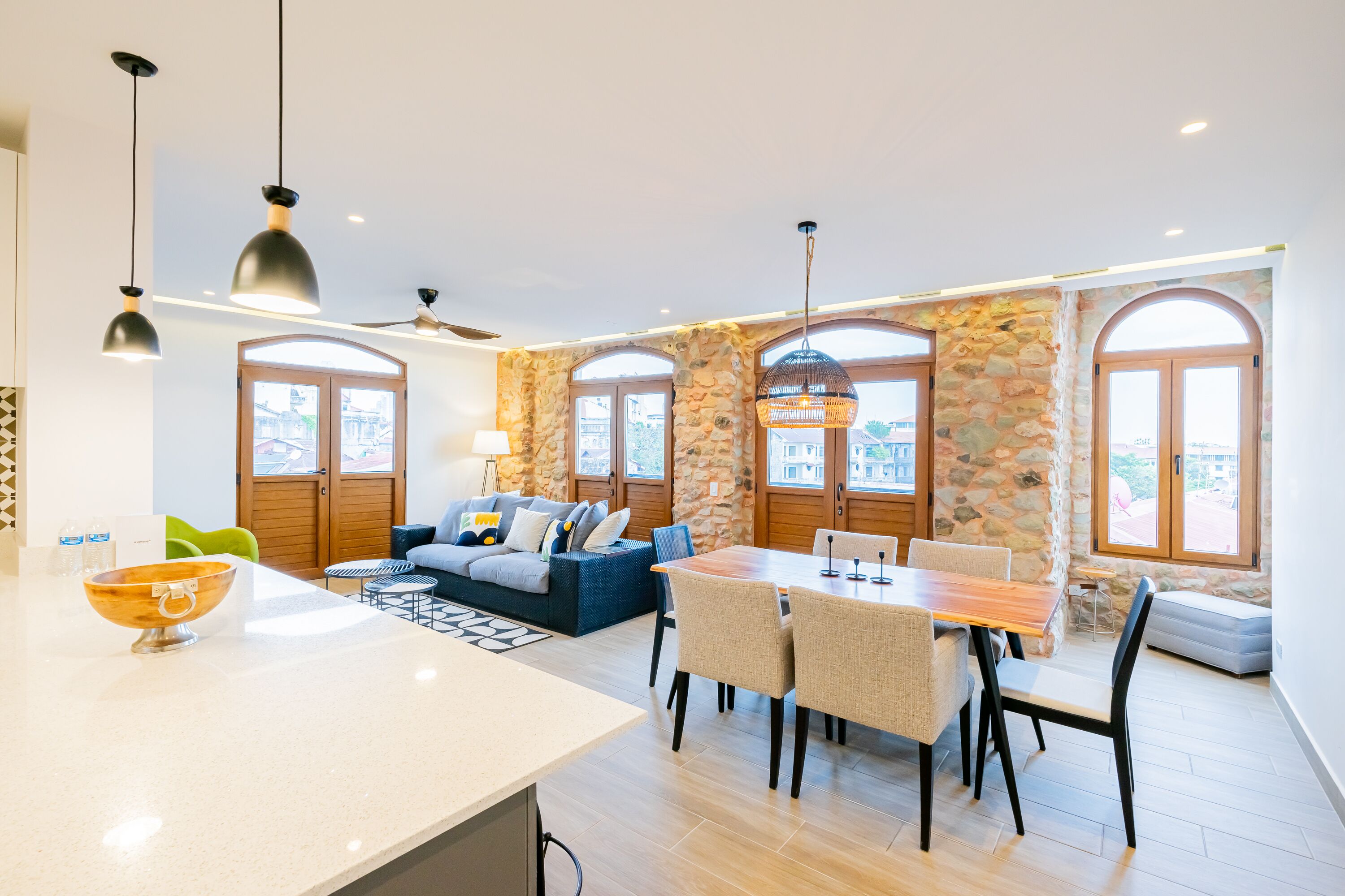 Een moderne woonkamer met een bank, eettafel en stoelen. Er zijn stenen muren en grote ramen.