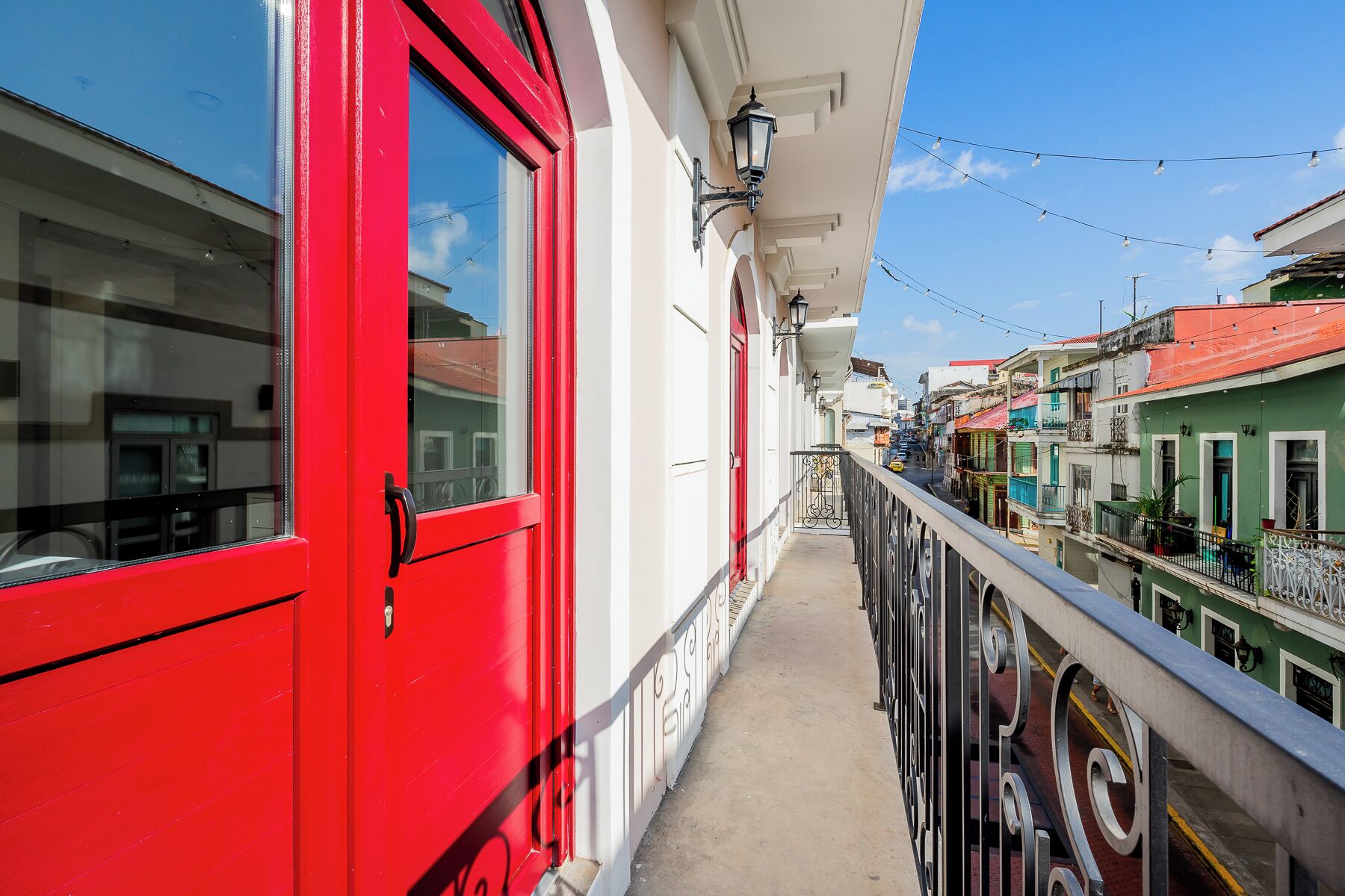 Un balcon étroit avec une porte rouge, des murs blancs et une rambarde en métal.