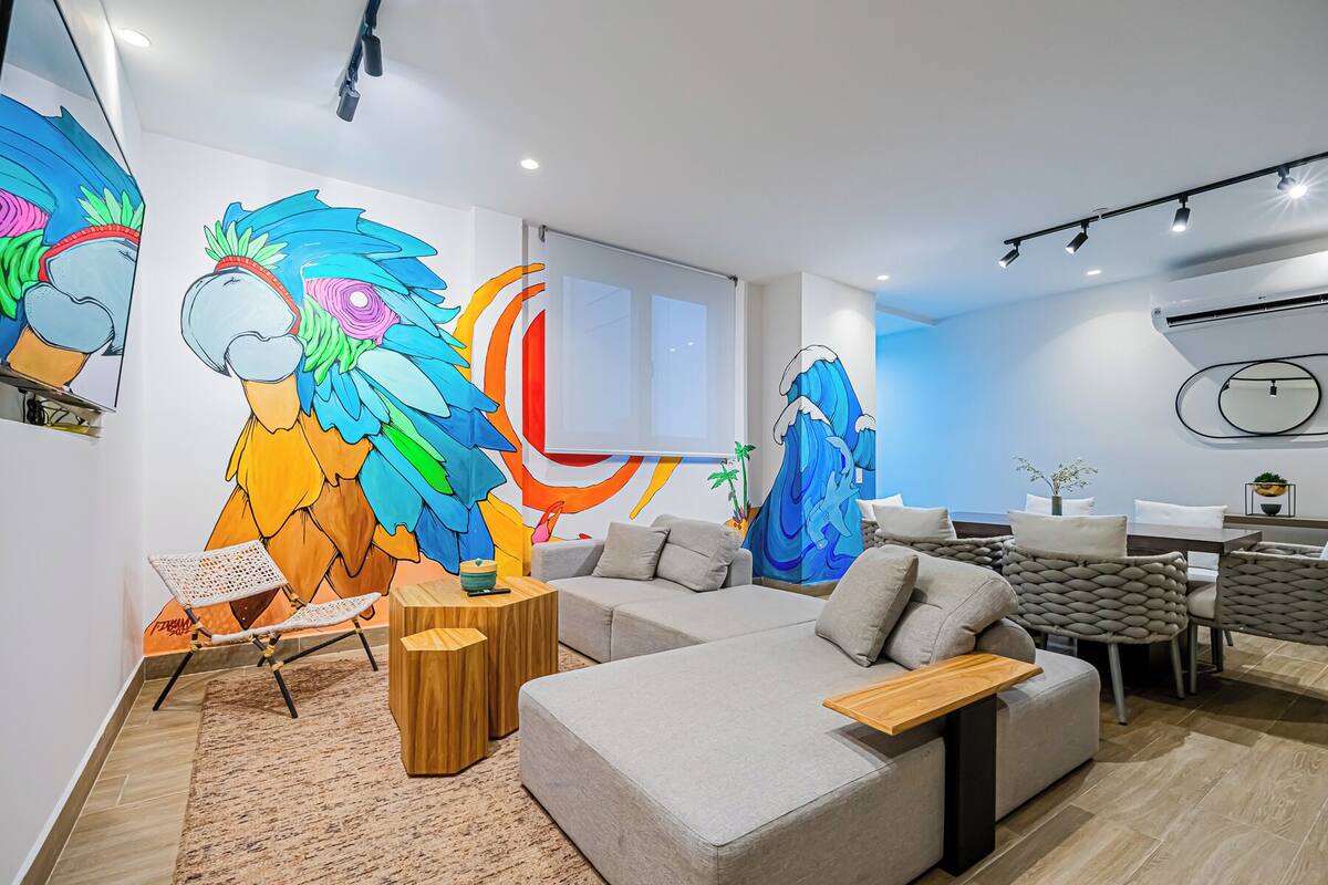 A modern living room with a sofa, coffee table, and a colorful mural on the wall.
