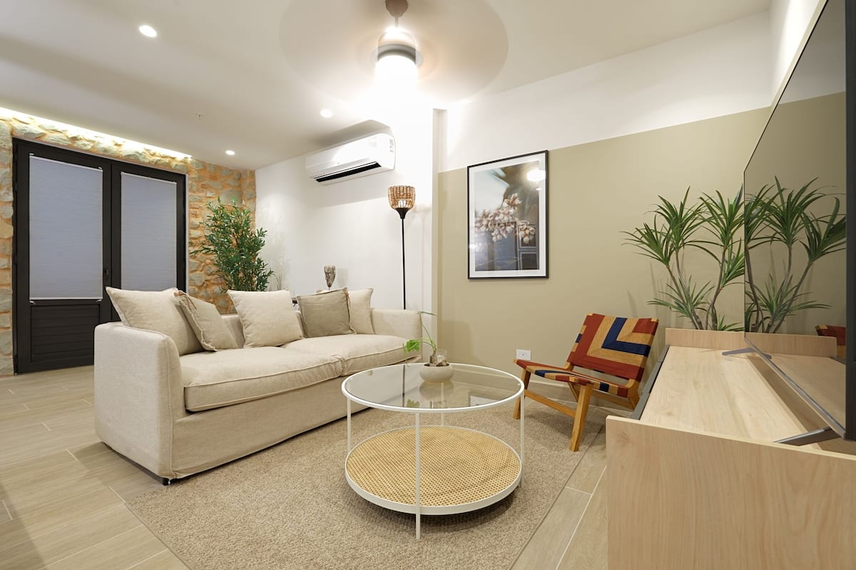 A modern living room with a sofa, a glass coffee table, a wooden side table, and a mirror.