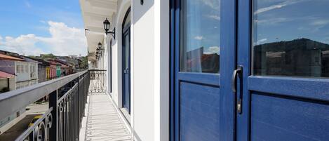 Un balcon avec une balustrade en métal, une porte bleue et un mur blanc orné d’une lanterne noire.