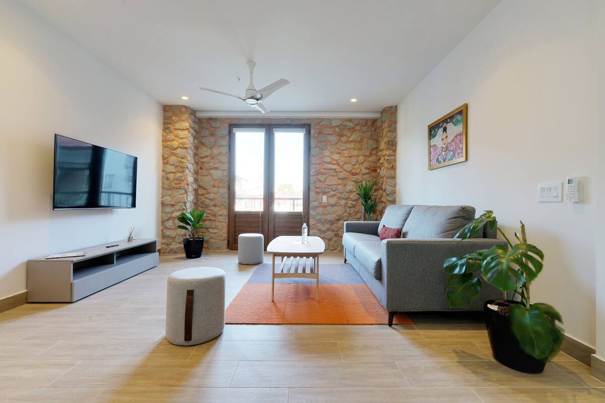 A modern living room with a flat-screen TV, a grey sofa, a coffee table, and a stone wall.
