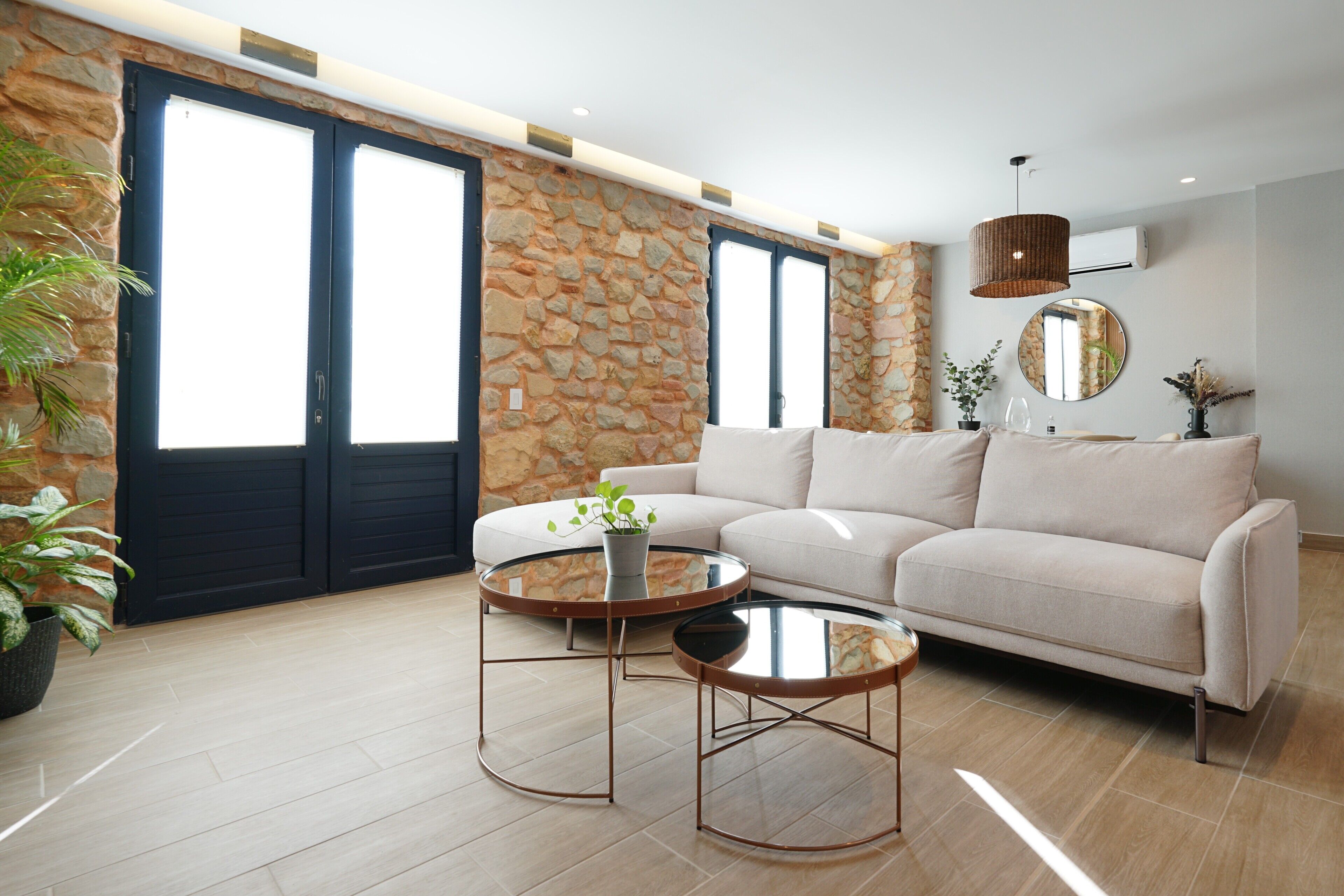 Ein modernes Wohnzimmer mit einer Steinwand, einem weißen Sofa, zwei runden Couchtischen und einem großen Fenster mit Aussicht.