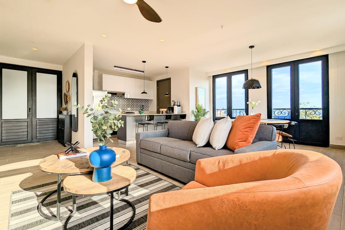 A modern living room with a grey sofa, orange armchair, and a blue vase on a round table.