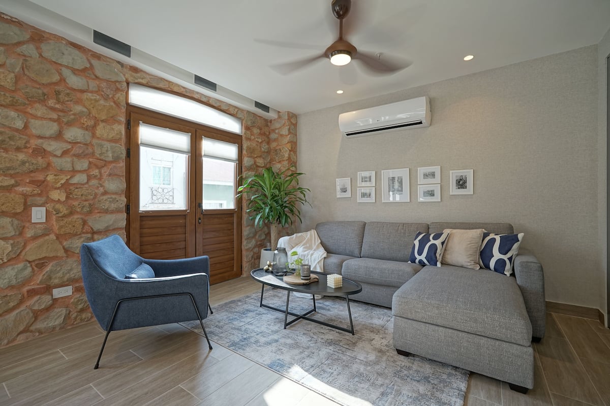A living room with a stone wall, a grey sofa, a blue armchair, a coffee table, and a ceiling fan.