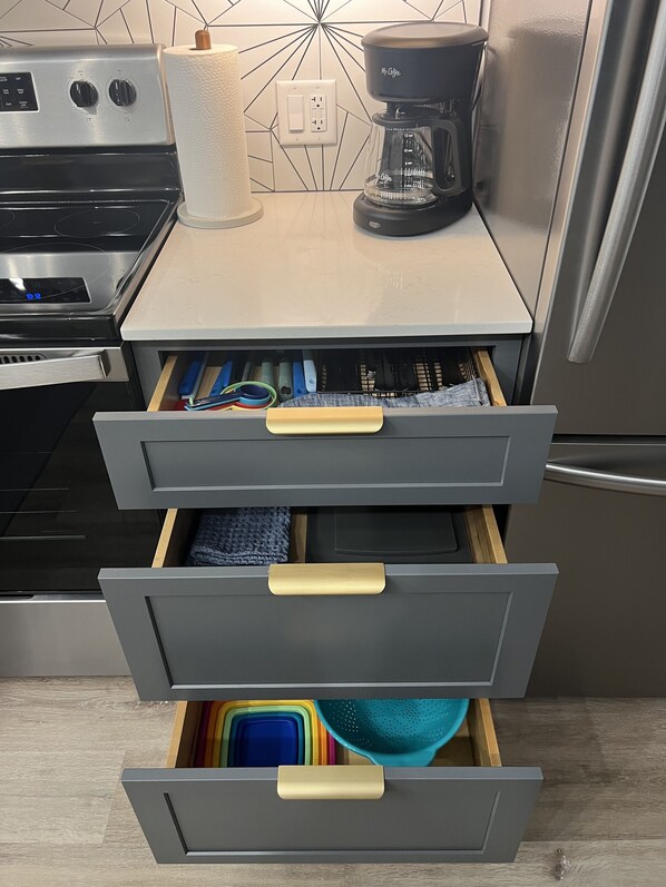 Una cocina con cafetera, dispensador de toallas de papel y un cajón con utensilios de cocina.