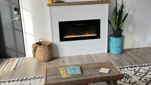 A living room with a fireplace, a television, a sofa, a coffee table, and a potted plant. - Cozy, Eclectic 1 BR Condo w/Rooftop Hot Tubs, Dog Friendly! (Traverse City)