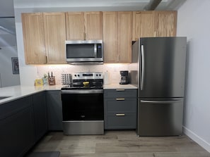 A modern kitchen with wooden cabinets, a stainless steel microwave, a built-in oven, a refrigerator, and a coffee maker on the countertop.