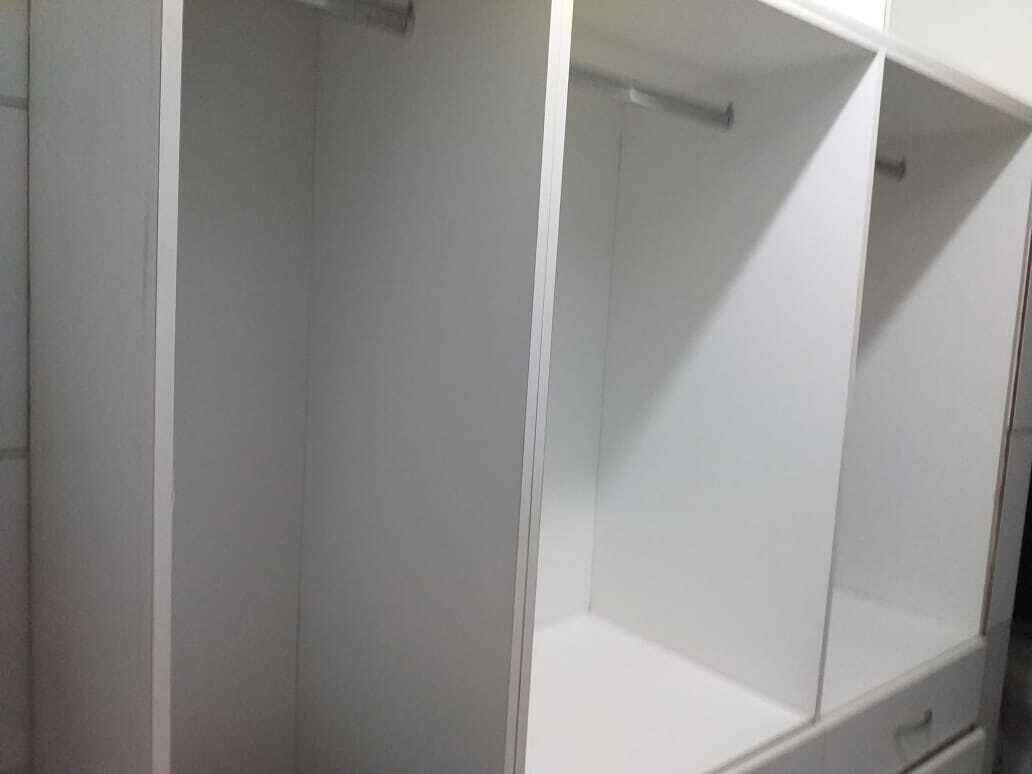 Ein weißes Zimmer mit einem Bett, einem Nachttisch und einem Kleiderschrank.