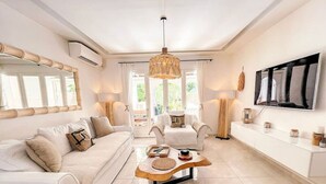 Una sala de estar moderna con un sofá blanco, una mesa de centro de madera y un televisor grande en la pared.