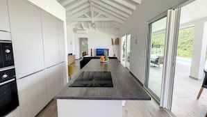 Eine moderne Küche mit weißen Schränken, einer schwarzen Arbeitsplatte und einer großen Kochinsel. Ein großes Schiebeglastür führt in einen Außenbereich mit einem Pool.