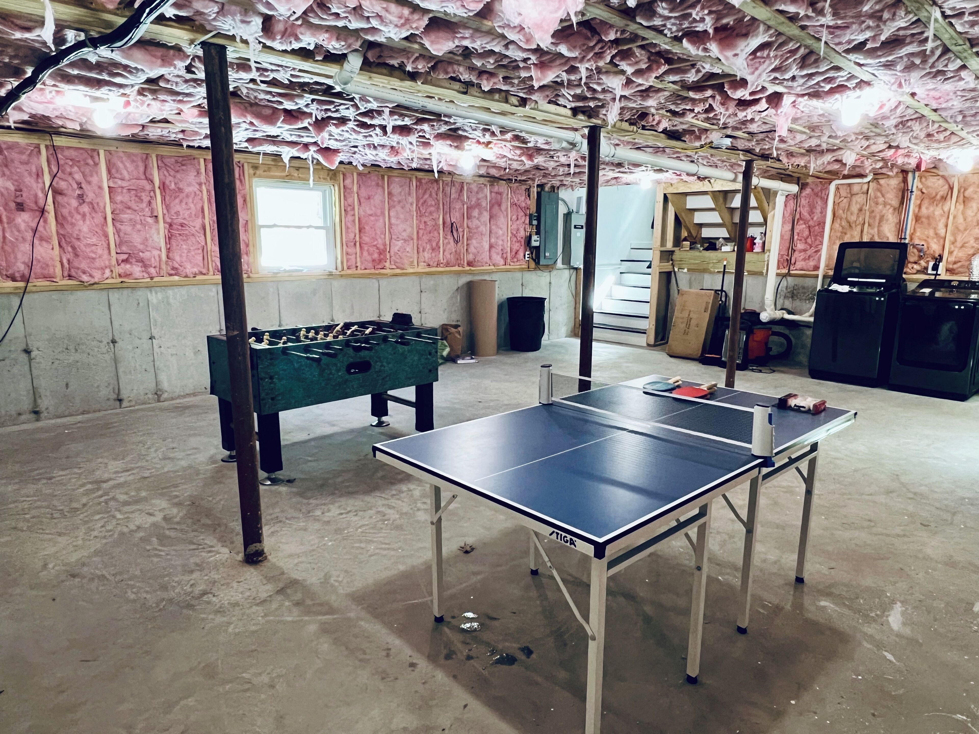 Una habitación con mesa de ping pong, mesa de fútbol y lavadora.
