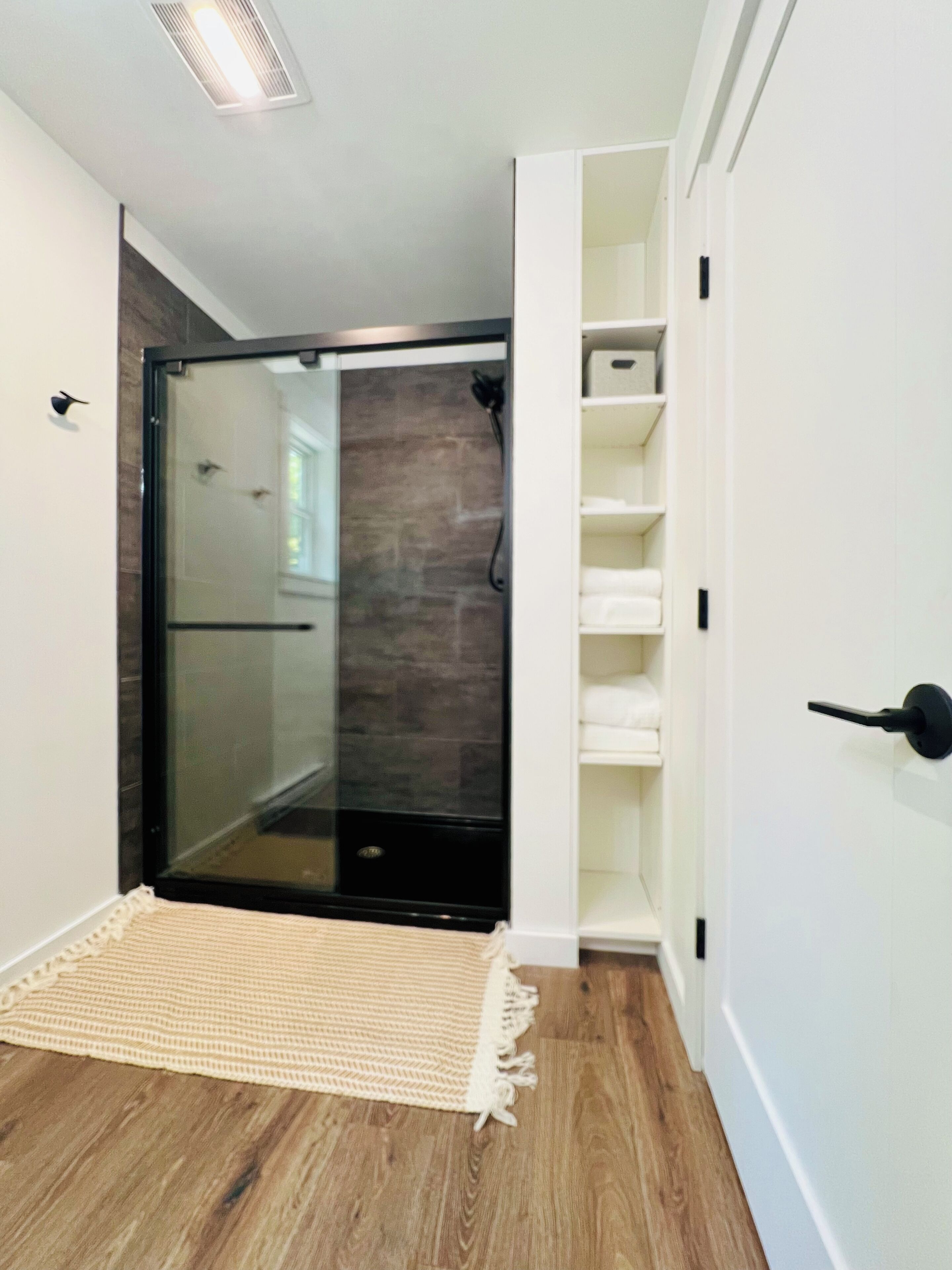 Ein modernes Badezimmer mit Duschabtrennung aus Glas, Holzboden und weißen Wänden.