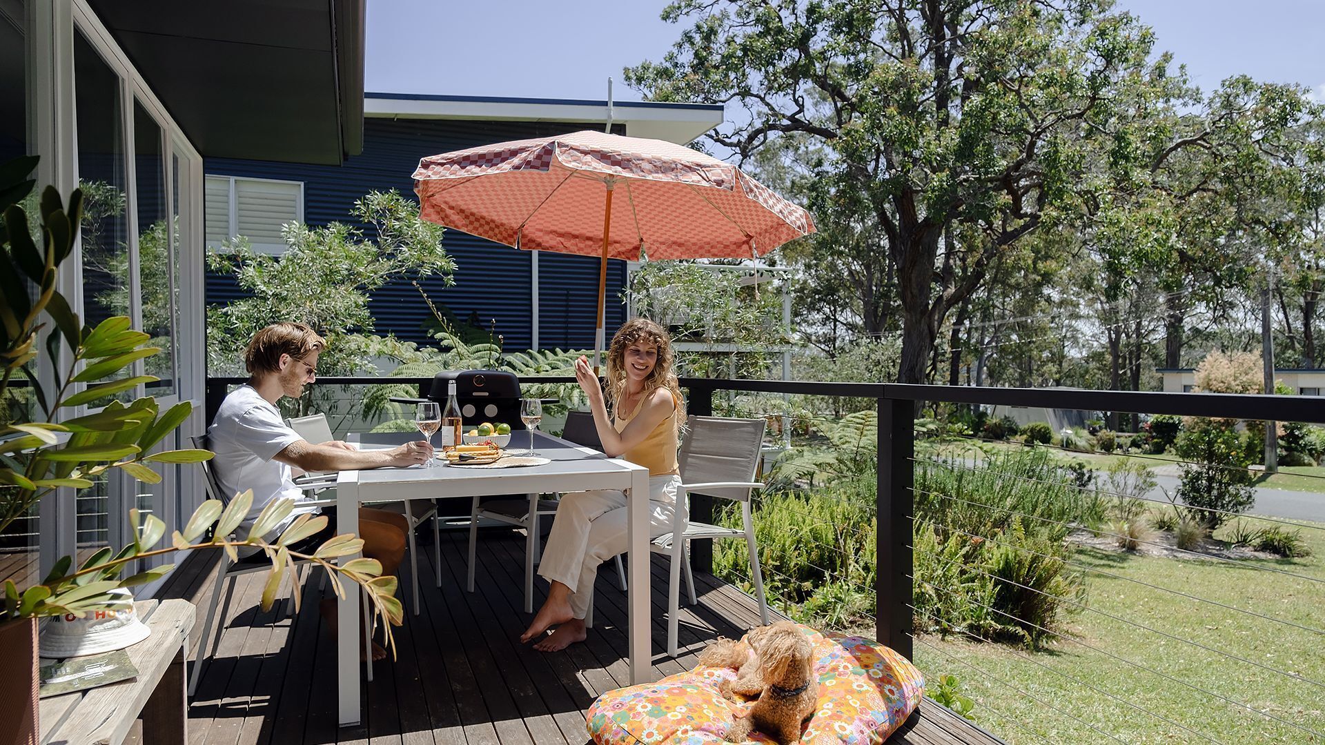 Een terras buiten met een tafel, stoelen, een barbecue en een hond die op een kussen ligt.