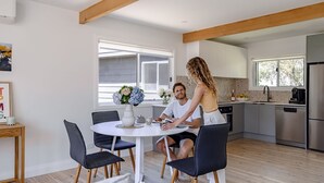 A modern kitchen with a dining area, featuring a round table, chairs, and a window providing natural light. - Little Miss Sunshine (Burrill Lake)