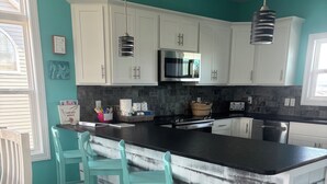 A kitchen with white cabinets, a black countertop, and teal chairs. - Amazing views, short walk to the beach, Pup friendly home in Surf City, NC! (Surf City)