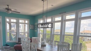A dining area with a wooden table and white chairs, large windows, and a ceiling fan. - Amazing views, short walk to the beach, Pup friendly home in Surf City, NC! (Surf City)