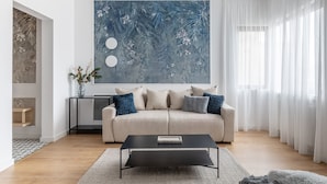 A modern living room with a beige sofa, a black coffee table, and a large abstract painting on the wall. - Luxury Piata Romana 2BR Urban Sanctuary by HOLT (Bucharest)