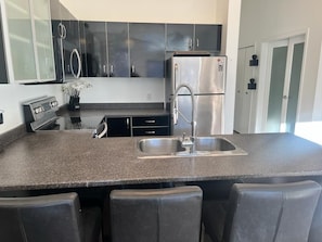 Eine Küche mit einem Edelstahl-Kühlschrank, einer doppelten Spüle und einem eingebauten Backofen. Vor der Spüle befinden sich drei Barhocker.