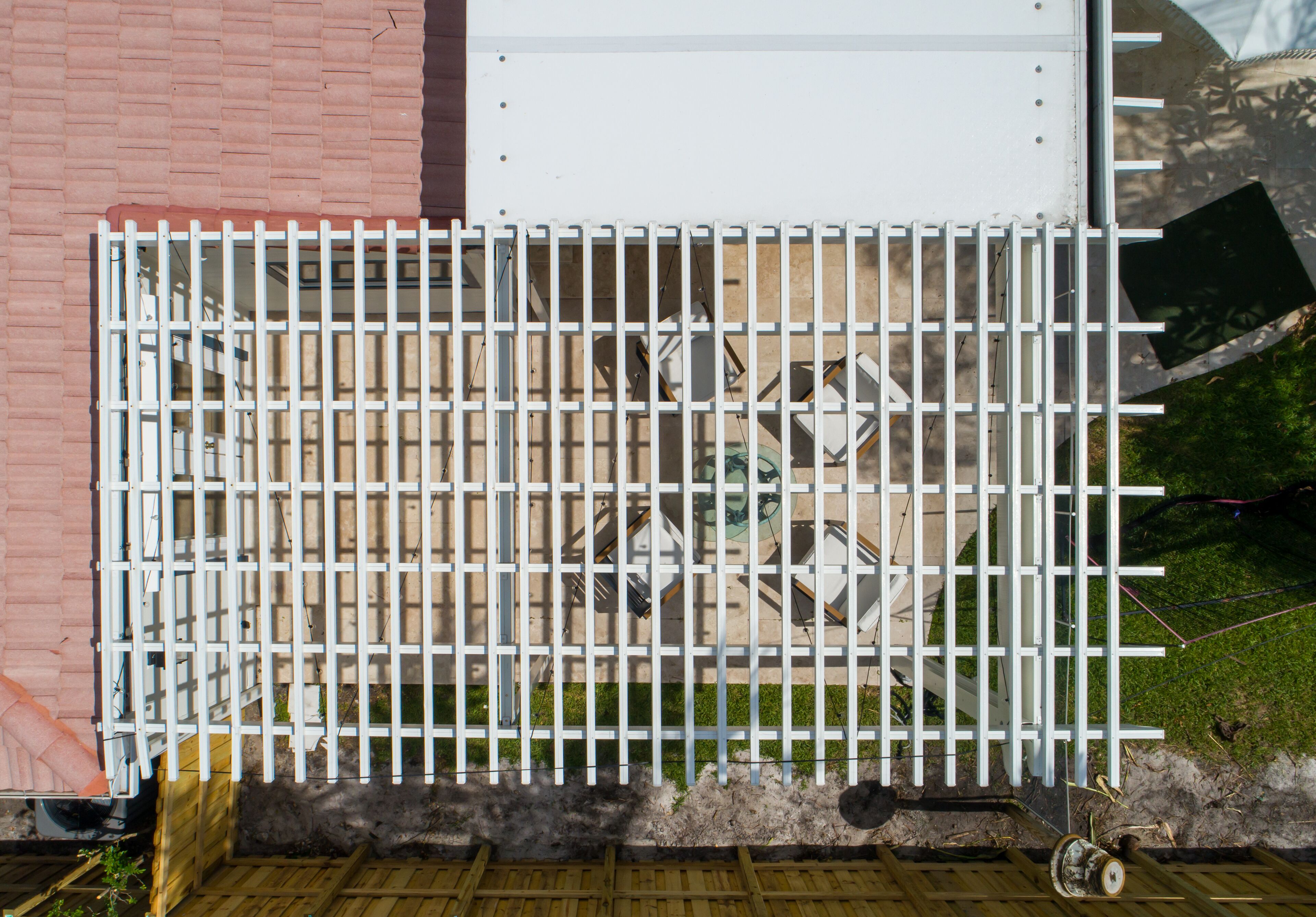 Ein weißes Metallgitter mit vertikalen Streben, eine Backsteinmauer und eine Holzdielen-Terrasse.