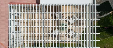 Ein weißes Metallgitter mit vertikalen Streben, eine Backsteinmauer und eine Holzdielen-Terrasse.