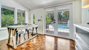 A spacious room with a wooden floor, a dining table with chairs, and a view of a swimming pool through glass doors. - Victoria Park Oasis with Heated Pool  (Fort Lauderdale)