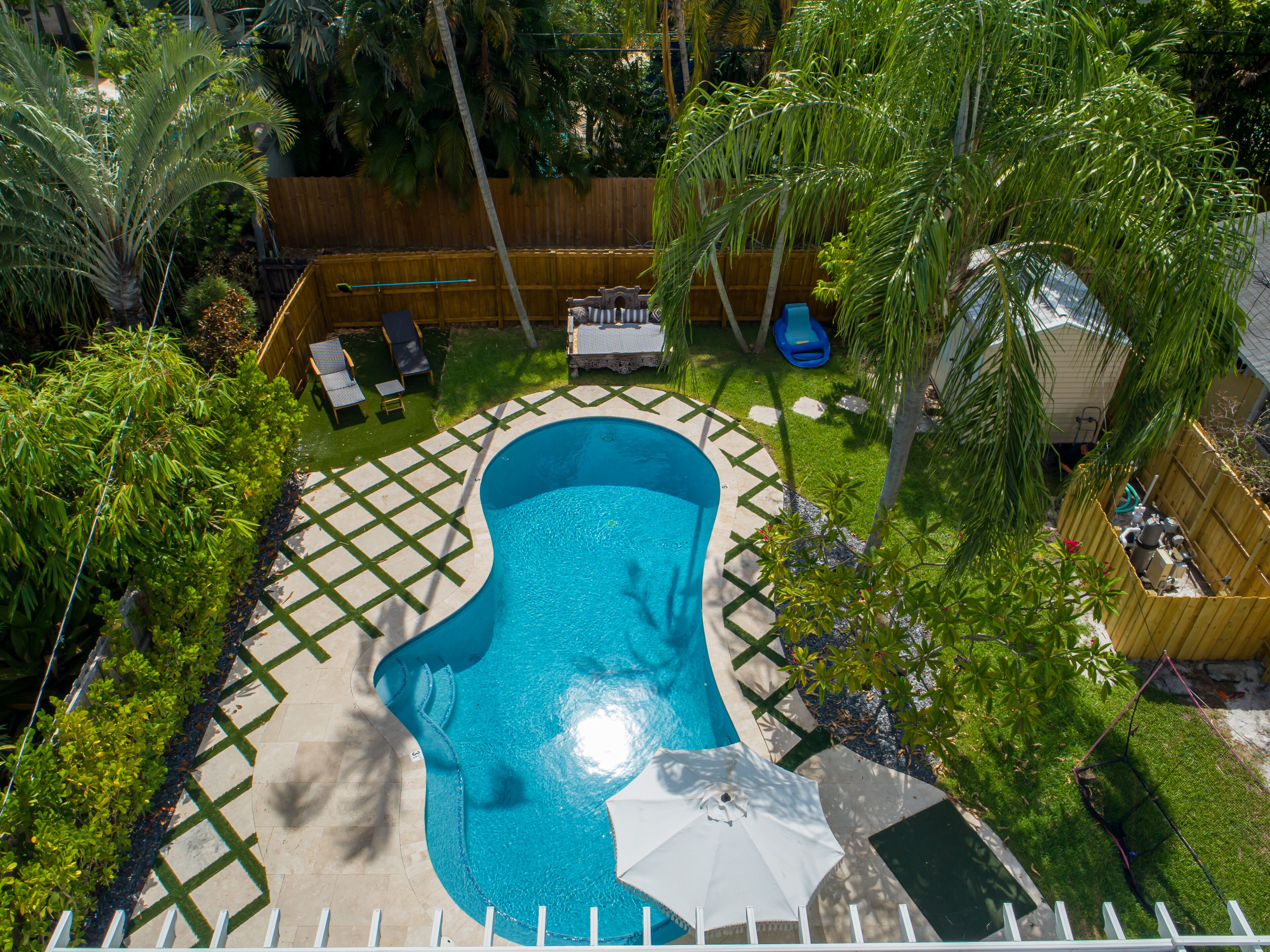 Un patio trasero con piscina, terraza de madera y un área cercada con hamaca y sillones de descanso.