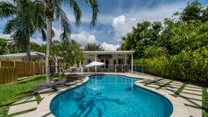 A swimming pool with a curved edge, surrounded by a stone deck and a wooden fence. - Victoria Park Oasis with Heated Pool  (Fort Lauderdale)