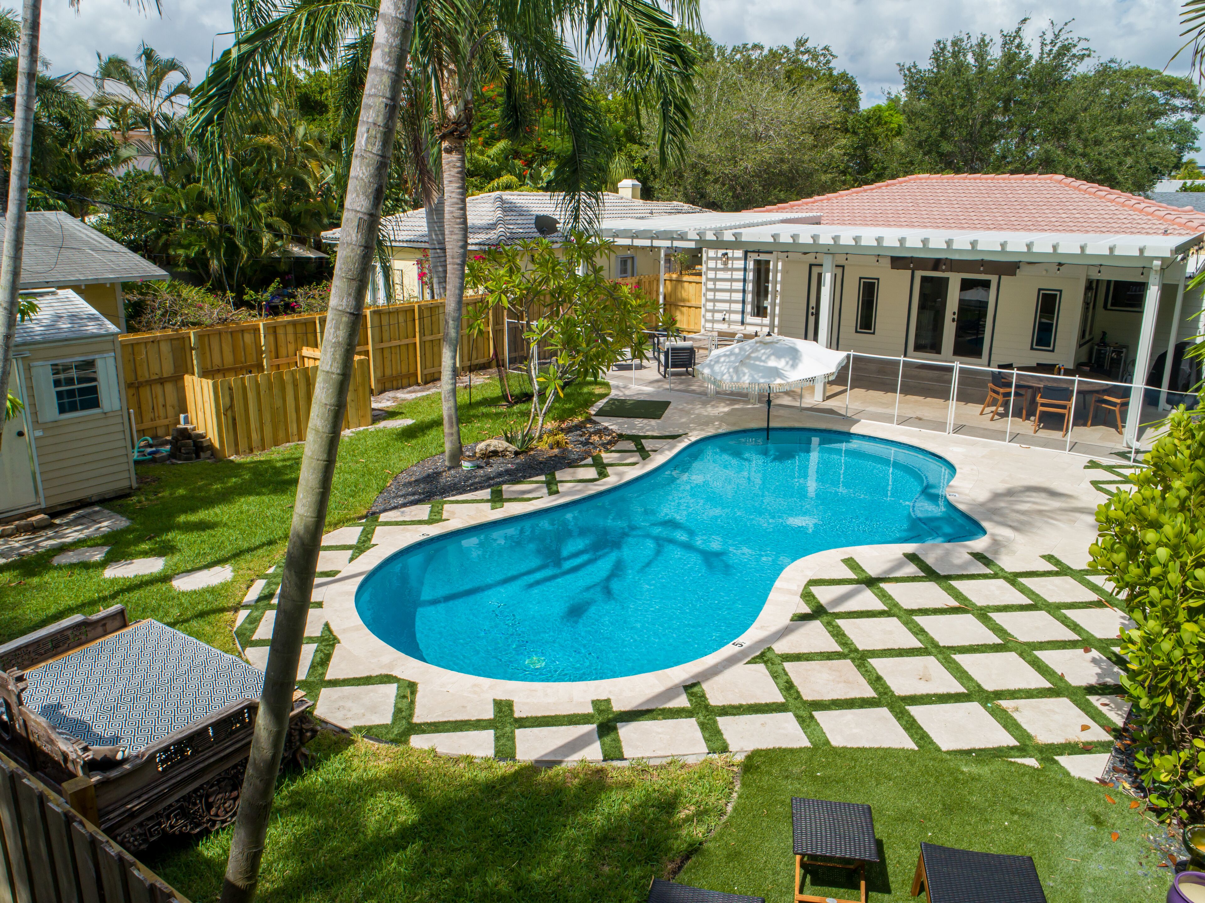 A backyard with a swimming pool, a patio with outdoor furniture, and a fenced area with a wooden deck.