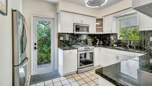 A modern kitchen with white cabinetry, a stainless steel refrigerator, a built-in microwave, and a gas stove. - Victoria Park Oasis with Heated Pool  (Fort Lauderdale)