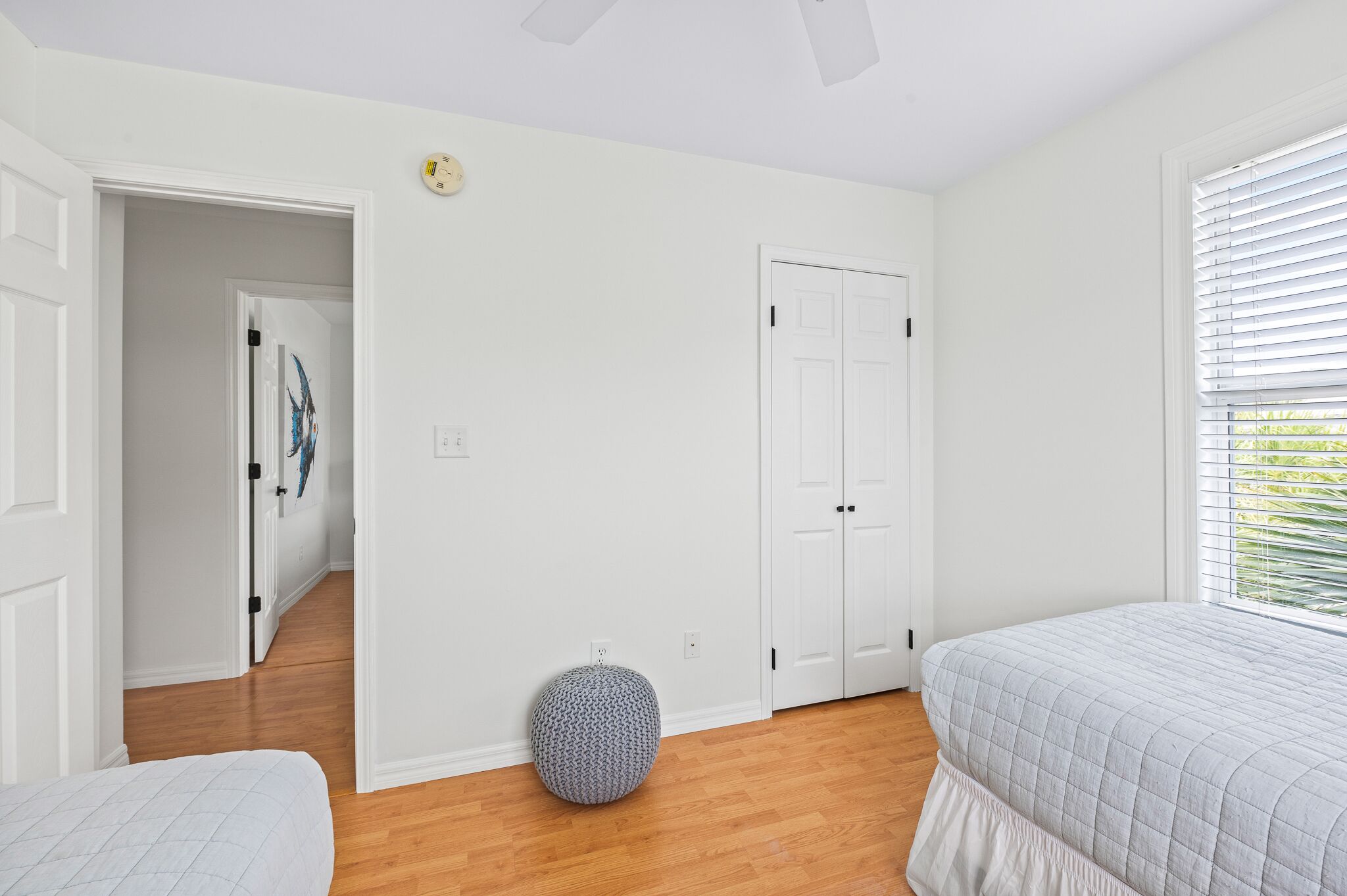 A bedroom with a bed, a round ottoman, a door, and a window with blinds.