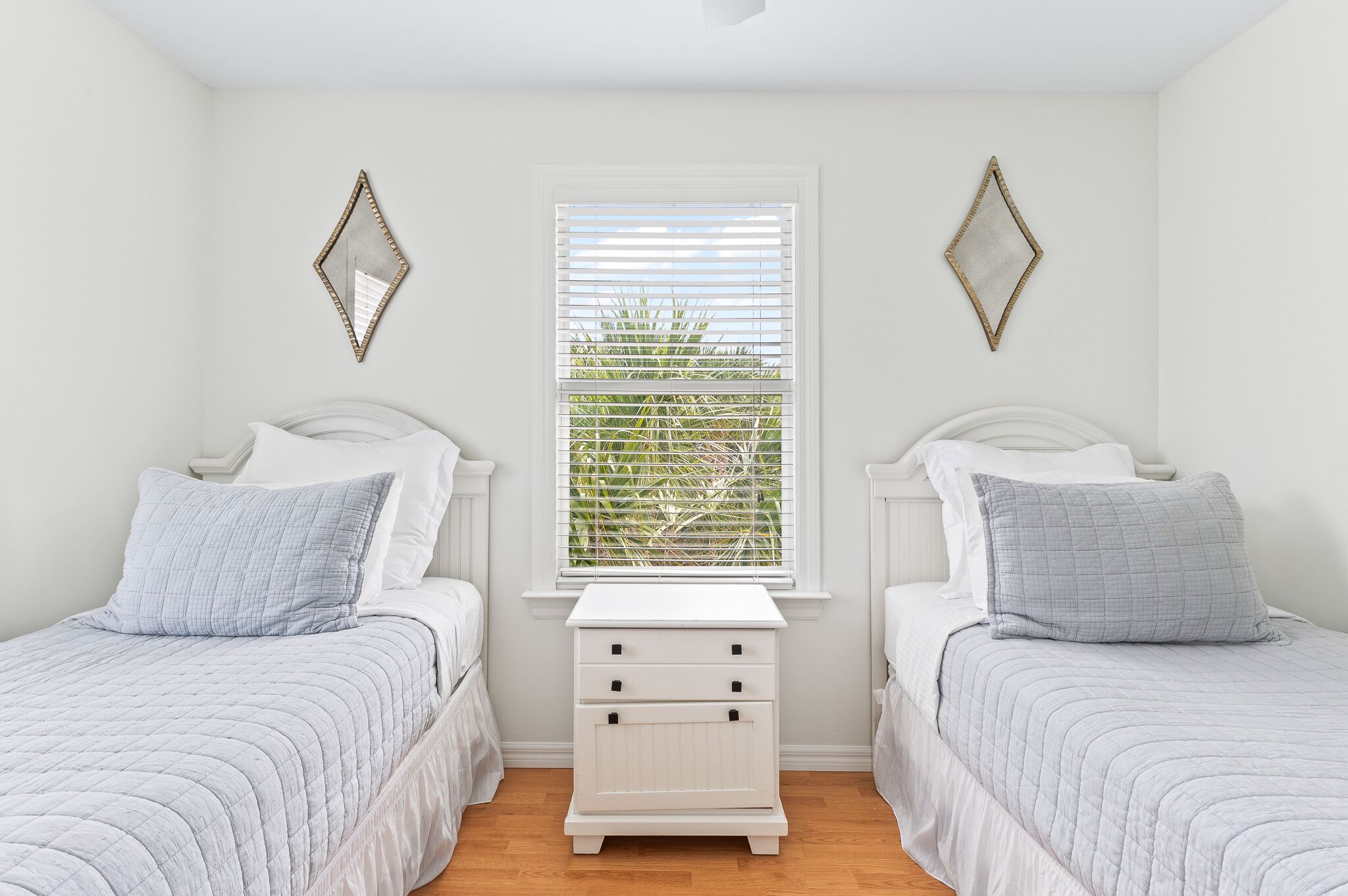 A bedroom with two beds, a nightstand, and a window with blinds.