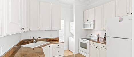 Una cocina moderna con gabinetes blancos, encimera de granito, horno empotrado y microondas.