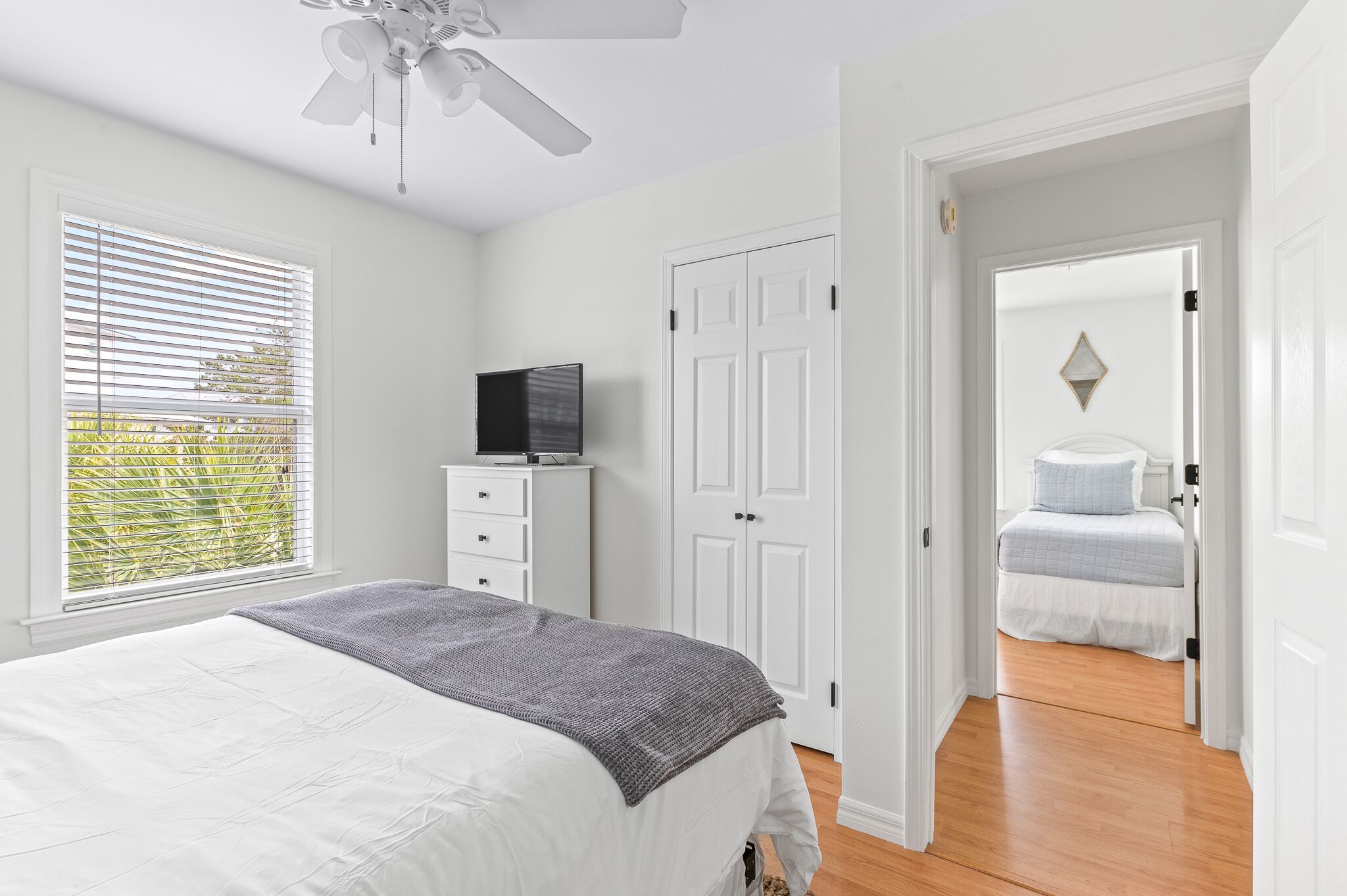 A bedroom with a bed, a TV on a dresser, a wardrobe, and a door leading to another room.