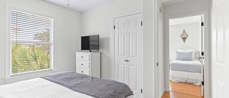 A bedroom with a bed, a TV on a dresser, a wardrobe, and a door leading to another room.