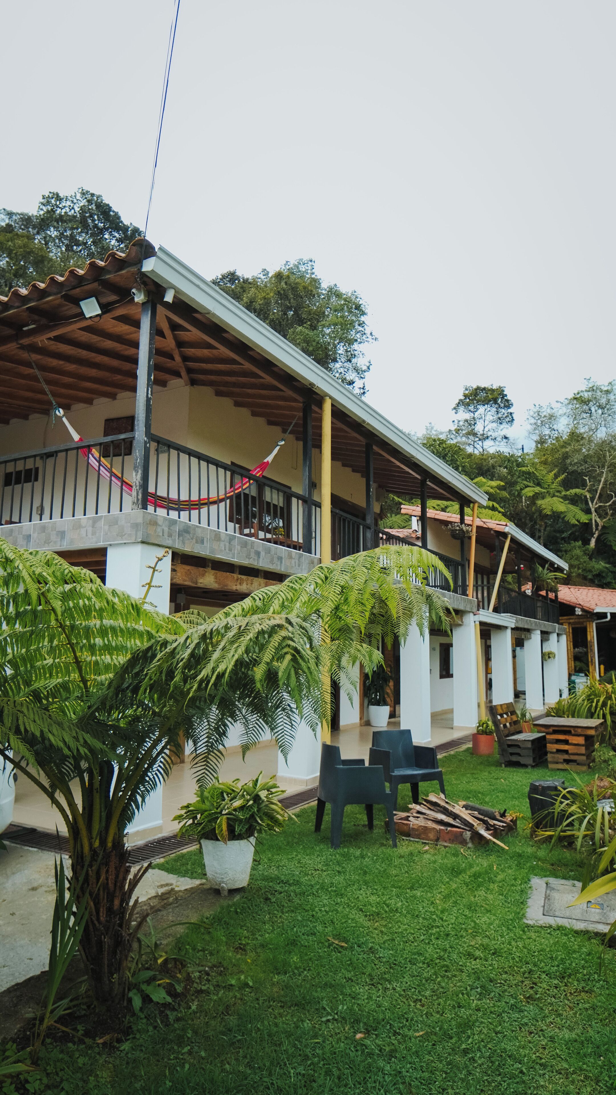 A two-story building with a covered patio area, outdoor seating, and lush greenery.