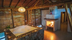 A stone bathtub with candles, a bamboo wall, and a fireplace.