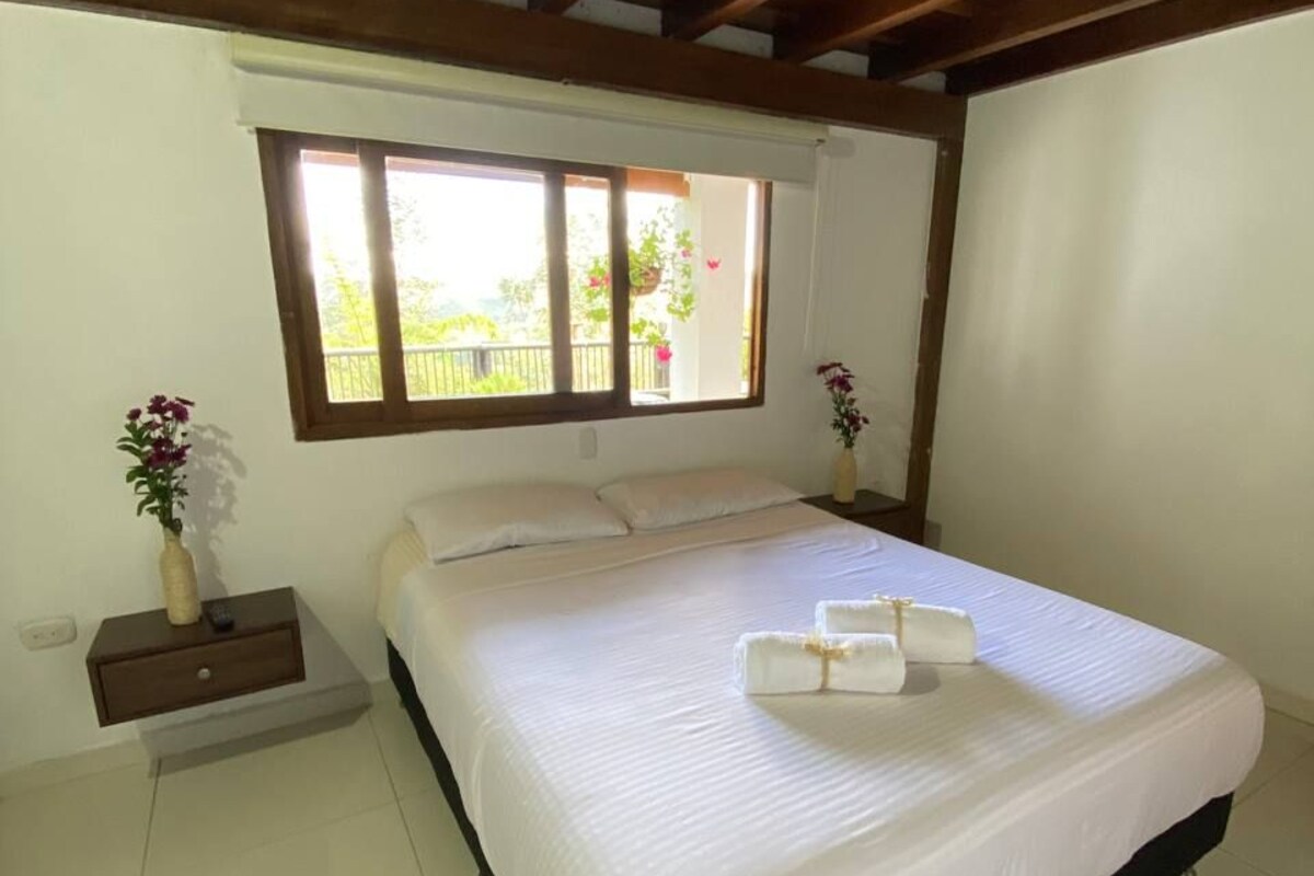 Een slaapkamer met een groot bed, houten balken in het plafond, een raam met uitzicht, een nachtkastje en een bedtafel.