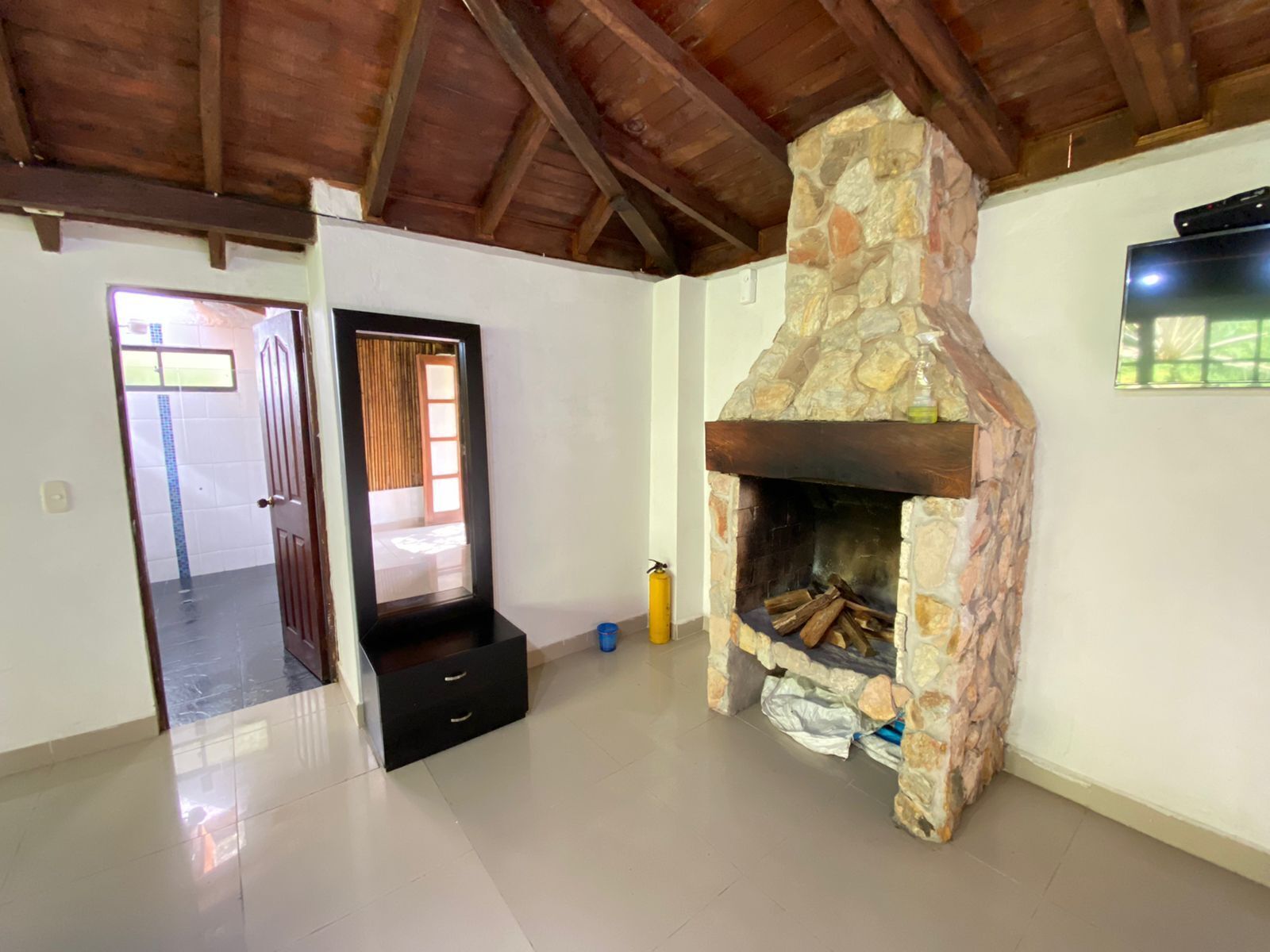 Une pièce dotée d’une cheminée en pierre, d’un plafond en bois et d’une porte donnant sur une autre pièce.