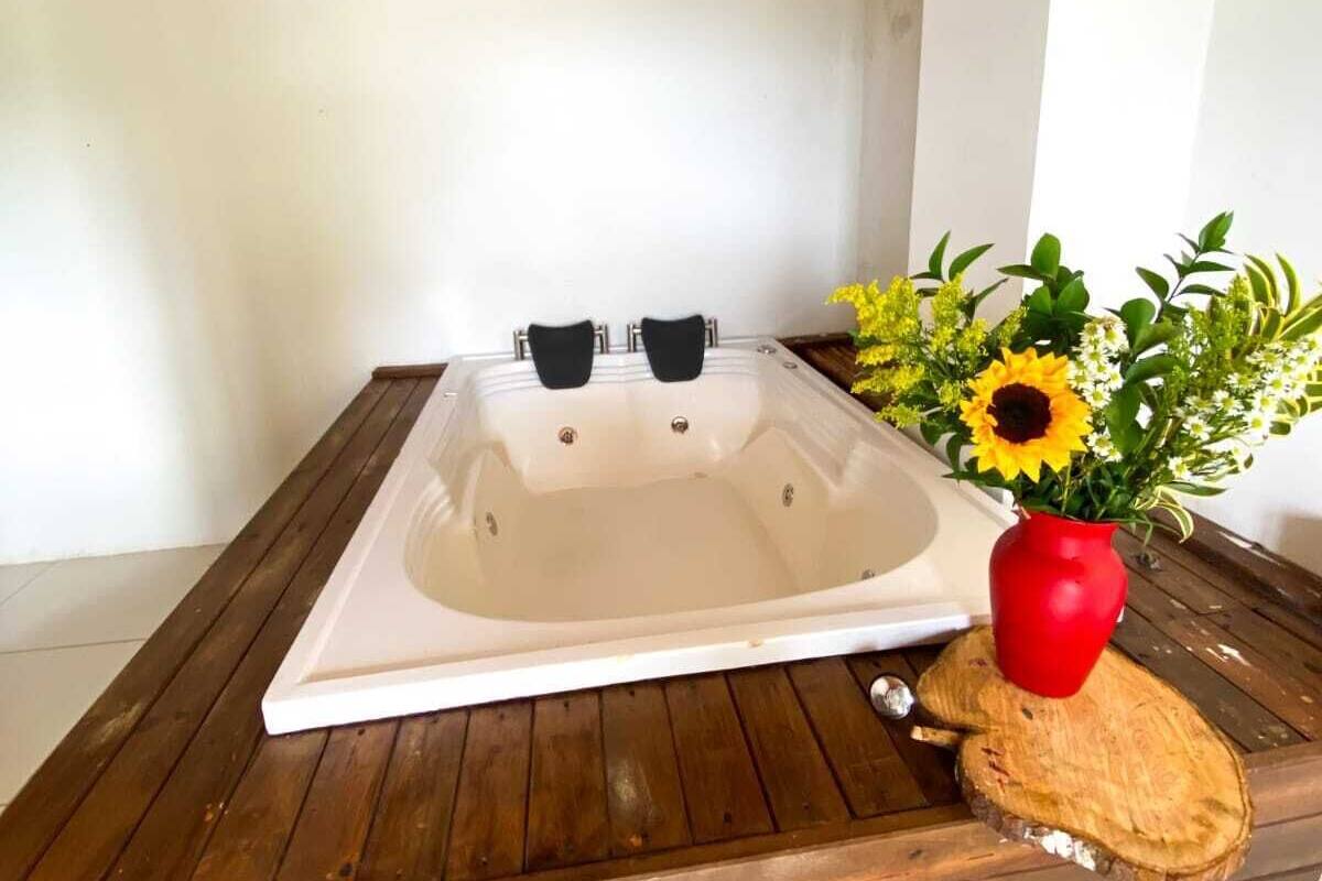 Un jacuzzi en una terraza de madera con techo de madera y una pared blanca al fondo.